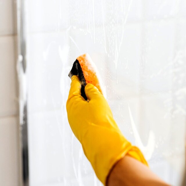 Gloved hand cleaning soap residue from shower glass