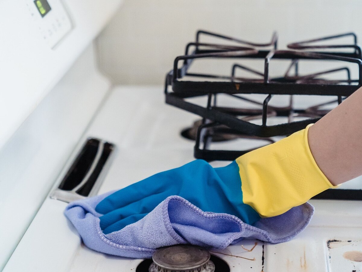 Gloved hands wiping residue from a gas stove surface