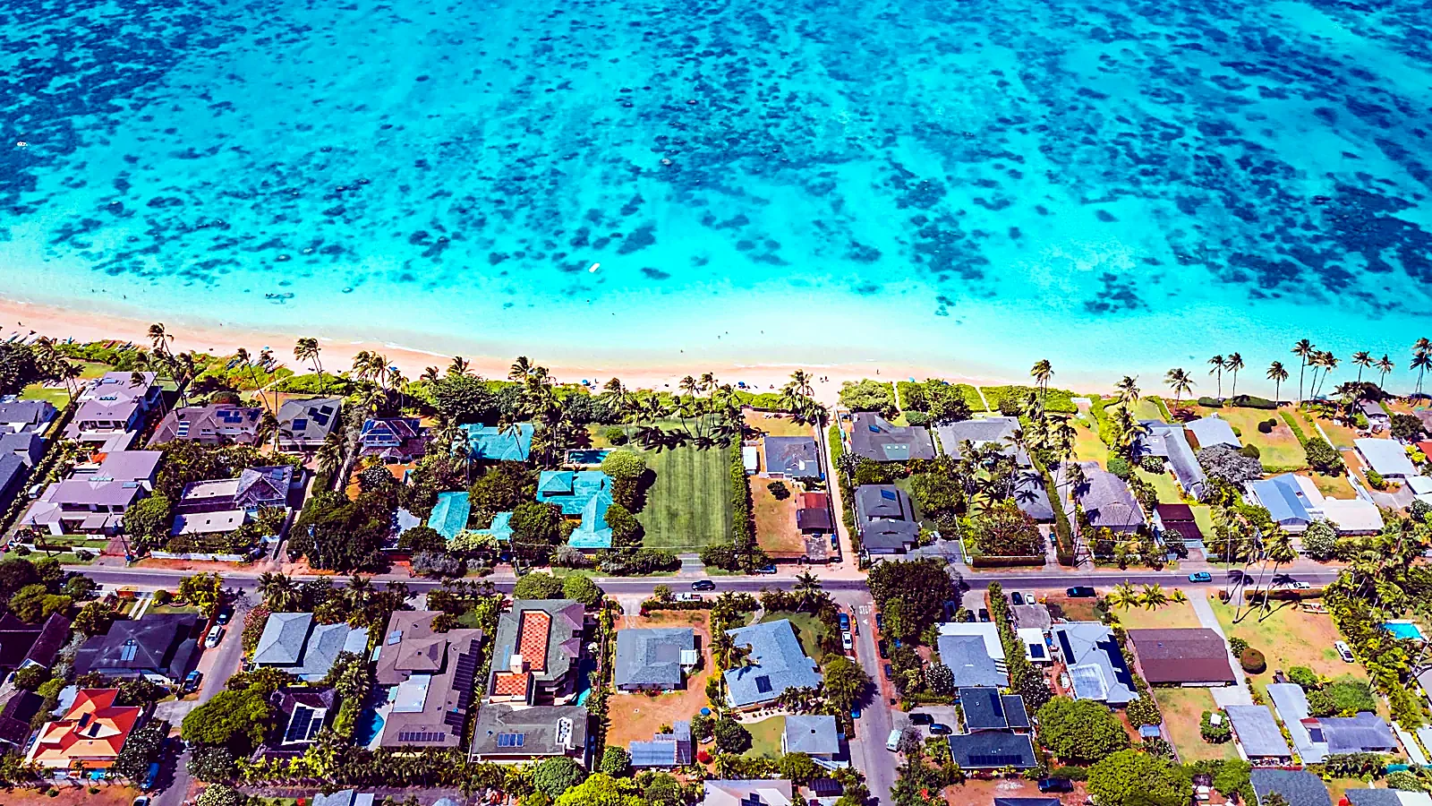 Aerial view of an Oʻahu shoreline neighborhood beside clear turquoise water