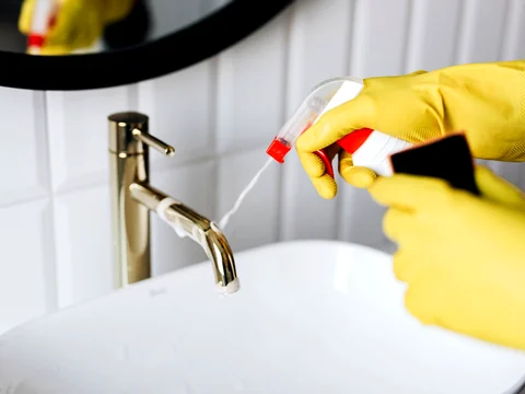 Gloved hand spraying and cleaning a bathroom faucet